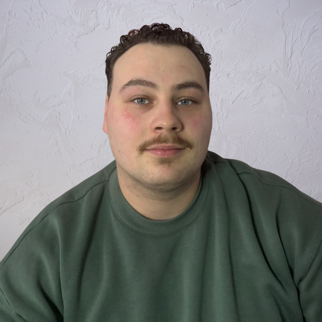 Über mich - Christoph Felgentreu - Schmetterlingskompass Junger Mann mit einem Schnurrbart, trägt ein grünes Sweatshirt, lächelt in die Kamera.